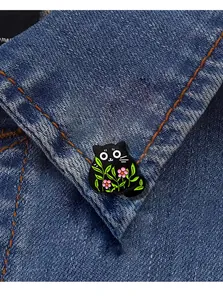 Detail of a black cat enamel pin with pink flowers pinned on a blue denim jacket collar