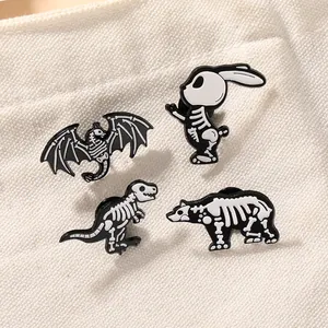 Lot de quatre broches en émail motif squelette de dinosaure et animaux en noir et blanc