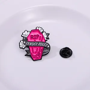 Detailed view of pink coffin enamel pin with RIP text and Gender Roles ribbon detail