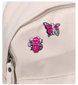 Detailed enamel pins featuring a pink RIP coffin and skeleton butterfly on a canvas backpack