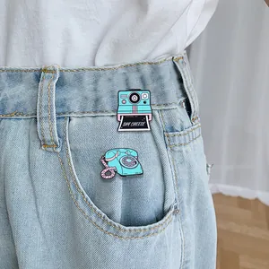 Set di spille in smalto con fotocamera retrò e telefono d'epoca su tessuto denim