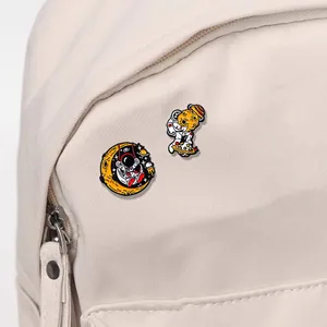 Detail of astronaut and moon enamel pins on a canvas bag showing craft texture