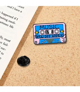 Close-up of pink and blue enamel music cassette tape pin on a textured cork background