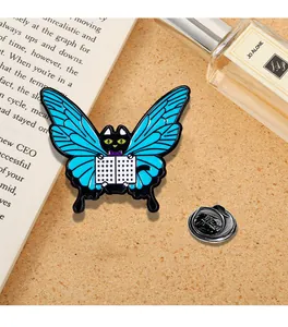 Dettaglio di una spilla smaltata a forma di gatto con ali blu e libro su sughero