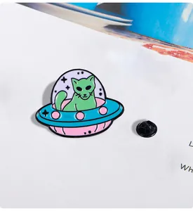 Detail of alien cat UFO enamel pin with bright green and pink finish on white card
