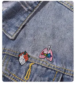 Detail von anatomischen Herz- und Lungen-Emaille-Pins an einer blauen Jeansjackentasche