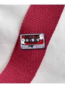 Detailed view of spooky cassette tape enamel pin with cute ghosts on white canvas