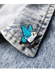 Dettaglio macro della spilla gatto in smalto con ali di farfalla blu su denim