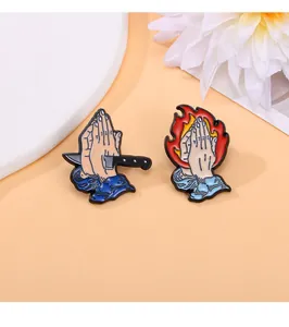 Detail view of cartoon enamel pins featuring praying hands with knife and fire designs