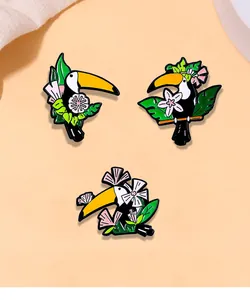 Détail de trois épinglettes toucan en émail avec motifs de fleurs et feuilles tropicales
