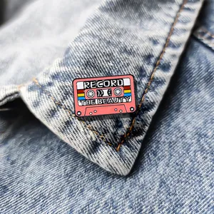 Vintage pink cassette enamel pin with Record The Beauty text on blue denim collar