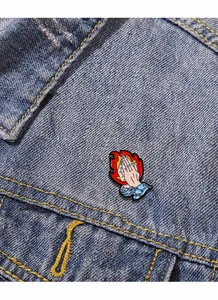 Macro shot of praying hands enamel pin with red flames pinned on blue denim fabric