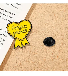 Macro d'une broche en émail cœur jaune avec le texte forgave yourself sur un fond en liège