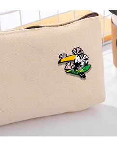 Détail d'un pin's émaillé toucan coloré avec fleurs sur un sac en toile beige