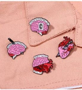 Detail von anatomischen Herz- und Hirn-Emaille-Pins auf rosa Jeansstoff mit Slogans