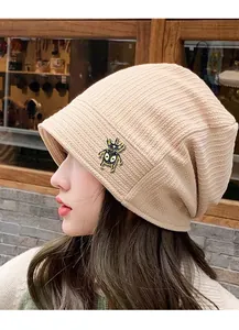 Detail of a beige knit beanie featuring a vintage gold and black beetle insect brooch