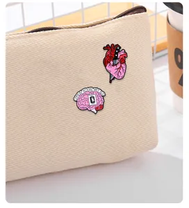 Detail von anatomischen Herz- und Gehirn-Emaille-Pins an einer Canvas-Tasche mit Design