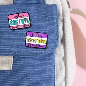 Emaille speldjes set met voornaamwoorden SHE/HER en THEY/THEM op een blauwe canvas tas