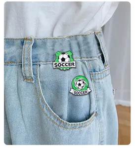 Dettaglio di due spille da calcio in smalto su una maglietta bianca e jeans