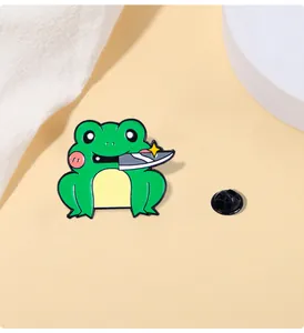 Close-up of a green cartoon frog enamel pin holding a knife with a black rubber back clasp
