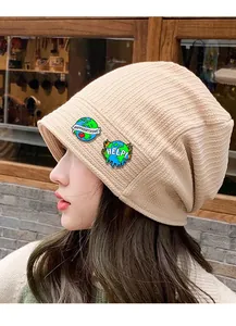 Detail of beige ribbed knit beanie featuring Happy Earth Day and Help enamel brooches