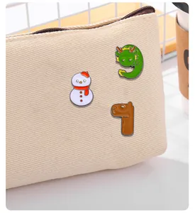 Dettaglio di spille in smalto con pupazzo di neve, drago e alpaca su una borsa di tela