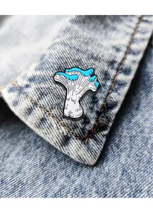 Detail of blue cartoon mushroom enamel pin on denim jacket collar with anthropomorphic face