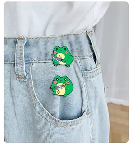 Close-up of cute cartoon frog enamel pins holding knives on denim jeans pocket