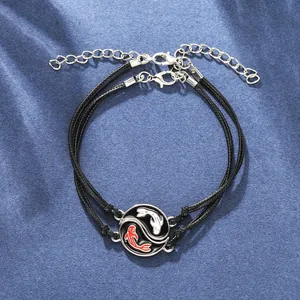 Detail of yin yang koi fish braided bracelets with black cord and silver clasp on blue silk