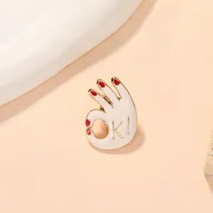 Detailed close-up of a white enamel OK gesture brooch with red nails and gold trim