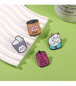 Quatre broches émaillées en forme de chats et boîtes de conserve sur un plateau texturé