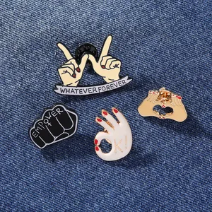 Close-up of four creative enamel lapel pins with various hand gestures on denim fabric