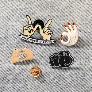 Detailed macro view of four creative enamel pins on denim, including OK and heart gestures