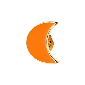 Detail of creative orange crescent moon enamel pin with polished gold metal edges