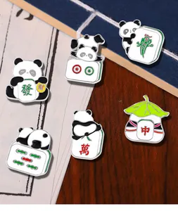 Close-up of enamel panda pins with mahjong tiles on a wooden background with accessories