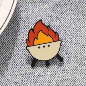Detailed close-up of a red BBQ grill enamel pin with fire on blue denim fabric