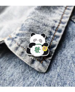 Detailed close-up of a cartoon panda enamel pin holding a Mahjong tile on denim fabric