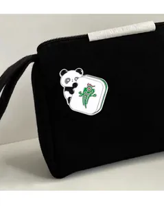 Close-up of enamel panda badge holding a mahjong tile on black canvas bag