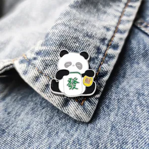 Cute panda enamel pin holding mahjong tiles on blue denim fabric background