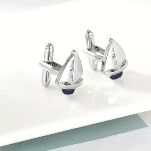 Detail view of silver sailboat cufflinks with blue enamel on a white ceramic tray