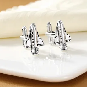 Silver airplane cufflinks with detailed wings and fuselage on a white ceramic plate