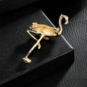 Broche flamant rose en métal doré avec émail posée sur un coffret à bijoux noir
