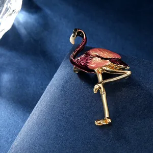 Gros plan d'une broche flamant rose avec ailes émaillées pourpres sur velours sombre