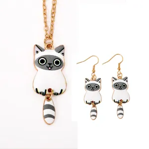 Detailed view of gold alloy cat pendant and hook earrings with white enamel finish