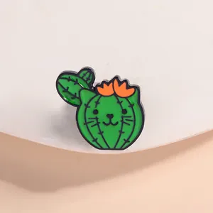 Close-up of a cute green cat-shaped cactus enamel pin on a white ceramic tray