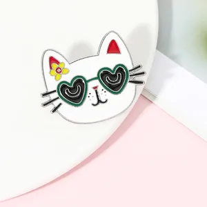 Detail of cartoon cat enamel pin with green heart glasses on soft pink background