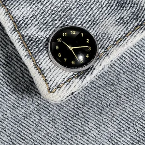 Macro-opname van een klokvormige broche met zwarte wijzerplaat en gouden cijfers op denim