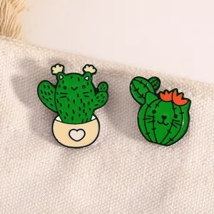 Detail of two creative green cactus cat enamel pins on textured white fabric