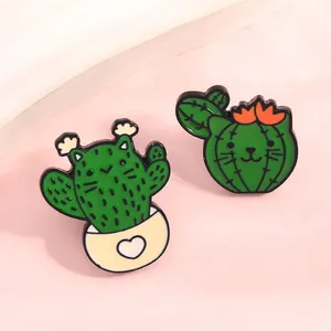Detailed macro shot of two cute cartoon cat cactus enamel pins on a pink surface