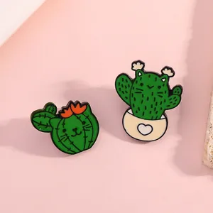 Detailed view of two green cartoon enamel pins featuring cat and cactus fusion designs